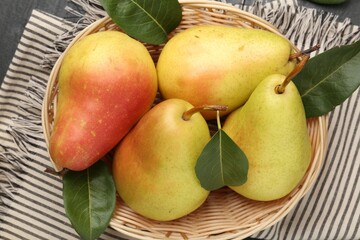 Many fresh pears and leaves in wicker bowl on black table, top view