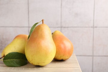 Many fresh pears and leaves on wooden table against light tiled wall, closeup. Space for text