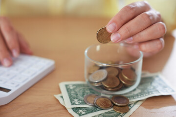 Woman with calculator putting money into jar at wooden table indoors, closeup