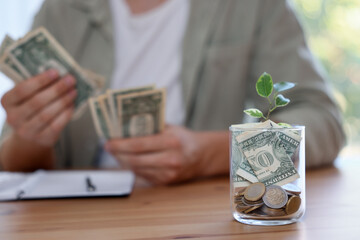 Glass jar with money and seedling. Man budgeting at desk, selective focus