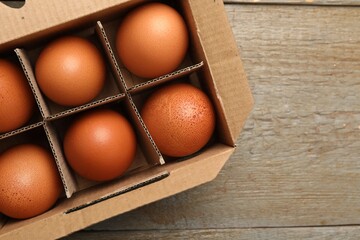 Raw chicken eggs in egg carton on wooden table, top view. Space for text