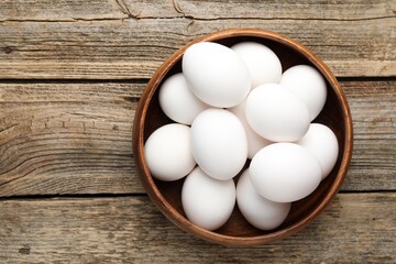 Fresh chicken eggs in bowl on wooden table, top view