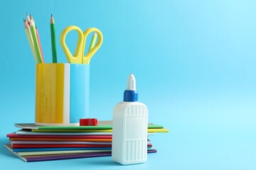Glue in bottle and other stationery on light blue background, closeup. Space for text