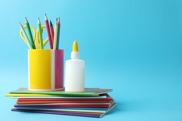 Fototapeta premium Glue in bottle, notebooks, color pencils and scissors on light blue background, closeup. Space for text