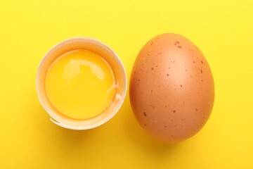 Whole and broken chicken eggs on yellow background, flat lay