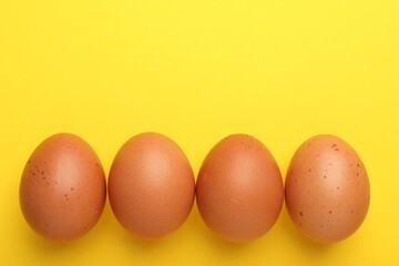 Raw chicken eggs on yellow background, flat lay. Space for text