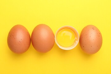 Whole and broken chicken eggs on yellow background, flat lay