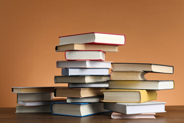 Stacks of many books on wooden table against light brown background