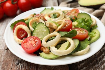 Delicious salad with squid rings and ingredients on wooden table, closeup