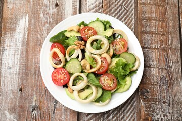 Delicious salad with squid rings, avocado, nuts and vegetables on wooden table, top view