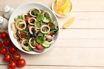 Delicious salad with squid rings and vegetables served on wooden table, flat lay. Space for text