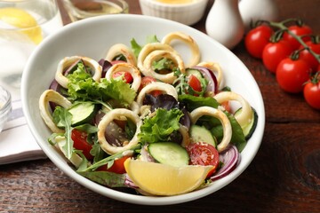 Delicious salad with squid rings and vegetables served on wooden table, closeup