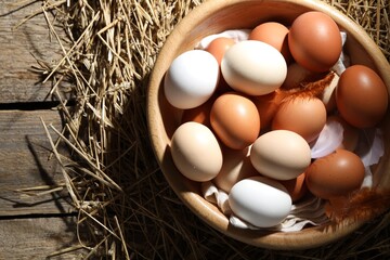 Raw chicken eggs, feathers and straw on wooden table, top view. Space for text