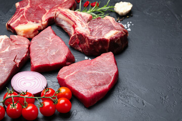 Pieces of raw beef meat, spices and tomatoes on black table, closeup. Space for text