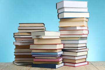 Many stacked books on wooden table against light blue background