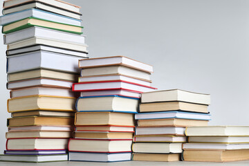Many stacked books on table against light grey background. Space for text