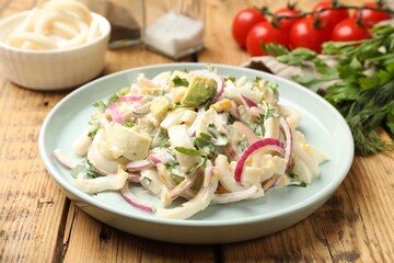 Tasty salad with squid rings, onion and eggs served on wooden table, closeup