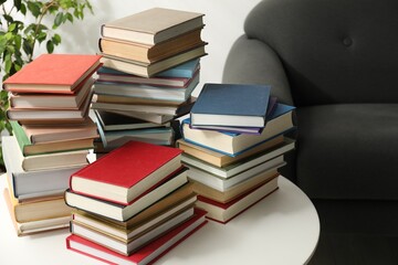 Many stacked books on white table and sofa indoors, closeup