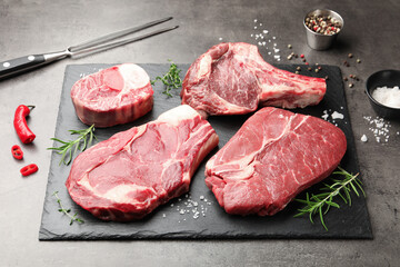 Pieces of raw beef meat, spices and carving fork on grey table, closeup