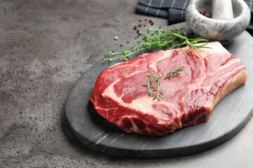 Piece of raw beef meat, spices, mortar and pestle on grey table, closeup. Space for text