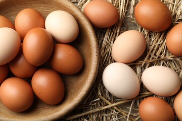 Raw chicken eggs in bowl and straw on table, flat lay