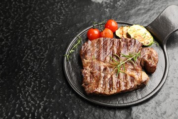 Delicious grilled beef steak with rosemary, zucchini and tomatoes on dark textured table. Space for text