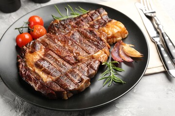 Delicious grilled beef steak with rosemary, onion, tomatoes and cutlery on grey textured table, closeup