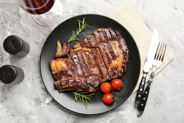 Delicious grilled beef steak with rosemary, onion and tomatoes served on grey textured table, flat lay