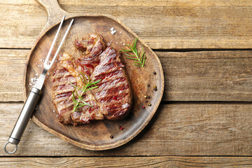 Delicious grilled beef steak with rosemary, spices and carving fork on wooden table, top view. Space for text