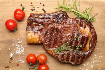 Delicious grilled beef steak with herbs, spices and tomatoes on wooden table, flat lay