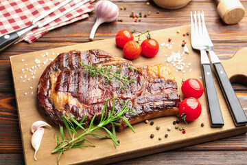 Delicious grilled beef steak with herbs, spices, products and cutlery on wooden table, closeup