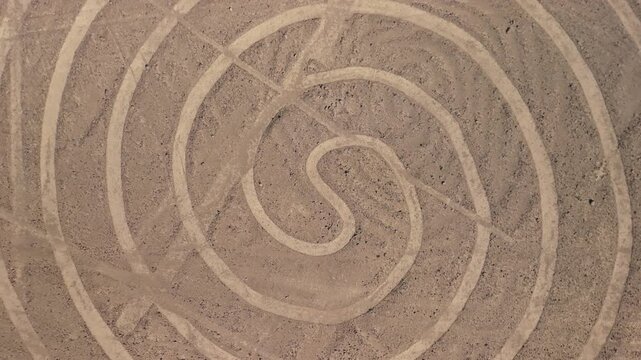 Fast aerial top down shot rising above the ancient spiral geoglyph one of the mysterious Nazca Lines etched into the desert plateau of Peru