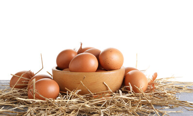 Raw chicken eggs, feathers, bowl and straw on grey wooden table against white background