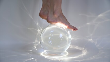 Delicate Balance: A Bare Foot Rests Precariously on a Gleaming Glass Sphere, Casting Dazzling Light Patterns.
