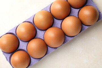 Raw chicken eggs in carton on light table, top view