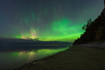 The magical green aurora borealis lights up the starry night sky over the calm Baltic Sea coast in...