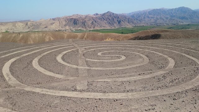 Aerial parallax shot of the spiral geoglyph among the Nazca Lines etched in the arid desert of southern Peru with mountain backdrop