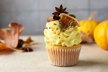 Delicious cupcake with color cream, spices and autumn decor on grey table, closeup