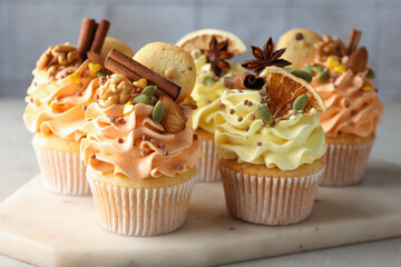 Delicious cupcakes with colorful cream, spices, cookies and nuts on grey table, closeup
