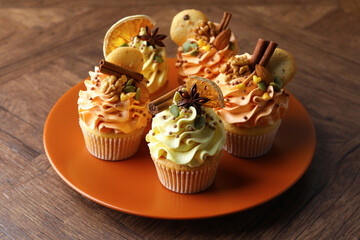Delicious cupcakes with colorful cream, spices, cookies and nuts on wooden table, closeup