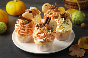 Delicious cupcakes with colorful cream, spices, nuts and autumn decor on grey table, closeup
