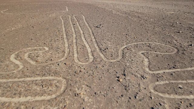 Descending aerial flight over the mysterious and ancient Nazca Lines geoglyphs with a slow tilt up revealing the vast desert landscape of Peru