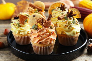 Delicious cupcakes with sprinkles, nuts and spices on wooden table, closeup. Autumn atmosphere