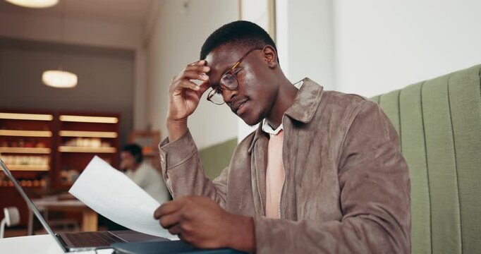 Reading, paperwork and black man with laptop in coffee shop, research and learning for scholarship. Education, glasses and college student with pc for studying, test review and class notes in cafe.