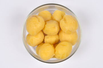 A glass bowl holds a pile of smooth, golden-yellow boiled potatoes that have been peeled, centered against a  white background