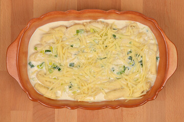 An oval ceramic baking dish with potato gnocchi and a creamy leek sauce generously covered with shredded cheese, prepared for baking