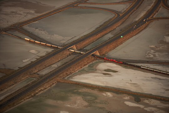 Aerial view of trains traversing the stark, geometric landscape of the salt ponds, their red and beige cars contrasting with the muted earth tones, Salt Lake City, Utah, United States.