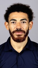 Fototapeta premium Man with curly dark hair and a beard poses for a close-up portrait in a plain background during daylight