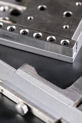 Close up of a precision linear motion guide rail with metal screws and a caliper on a black background.