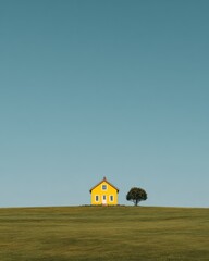 Bright yellow house stands alone on green hillside under clear blue sky